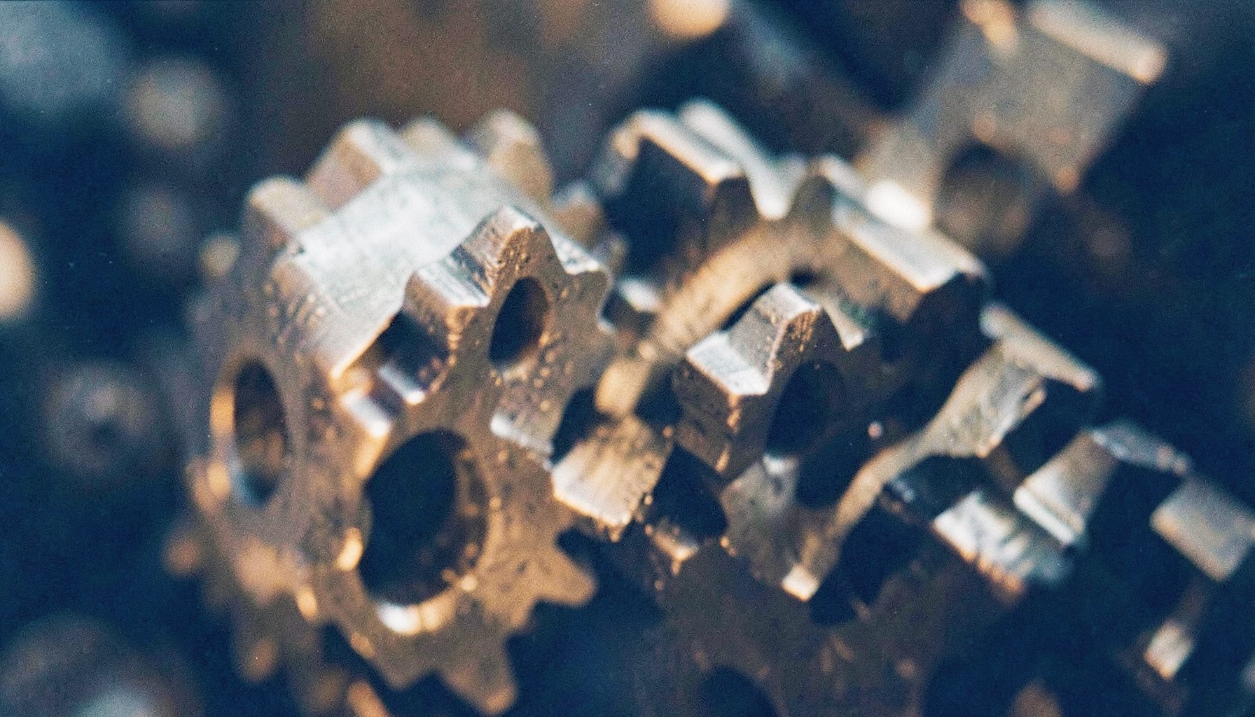Close-up of precision-machined metal automotive gears meshing together, warm amber and silver tones, shallow focus, visible film grain