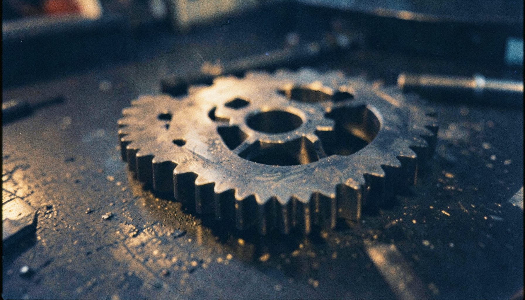 Analog photograph of precision-machined steel gears on a dark workbench, warm amber light catching the teeth