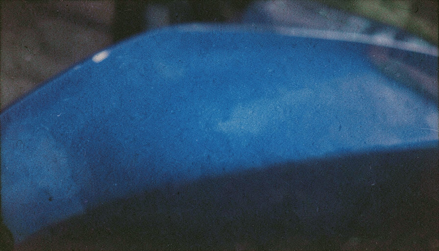 Grainy film close-up of a glossy automotive paint swatch panel in deep metallic blue, soft studio light